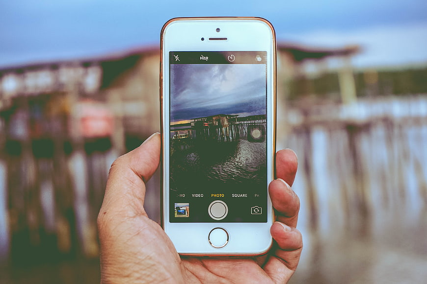Hand holding smartphone taking photo of pier at dusk