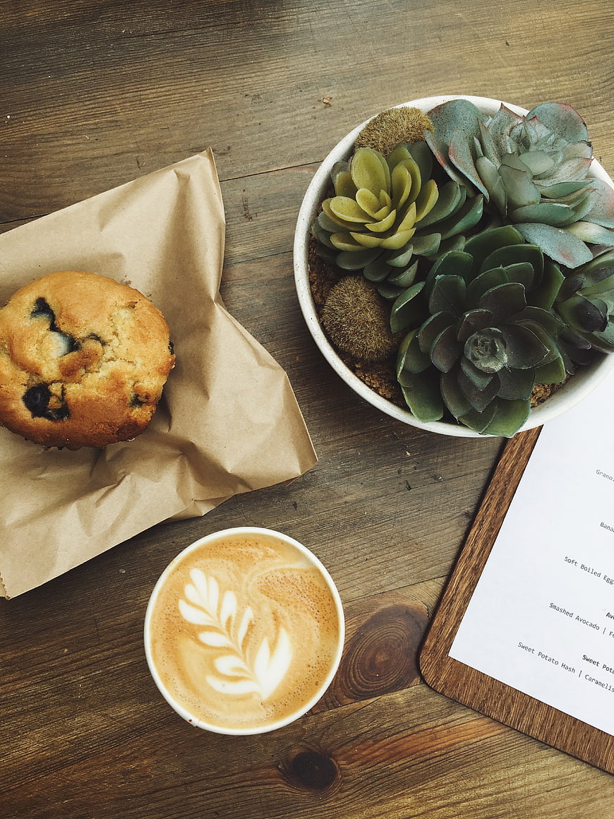 Flat lay of blueberry muffin, latte art coffee, and succulents on wood