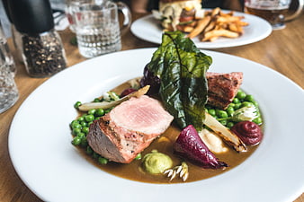 Seared pork tenderloin with peas, beetroot, and gravy on white plate