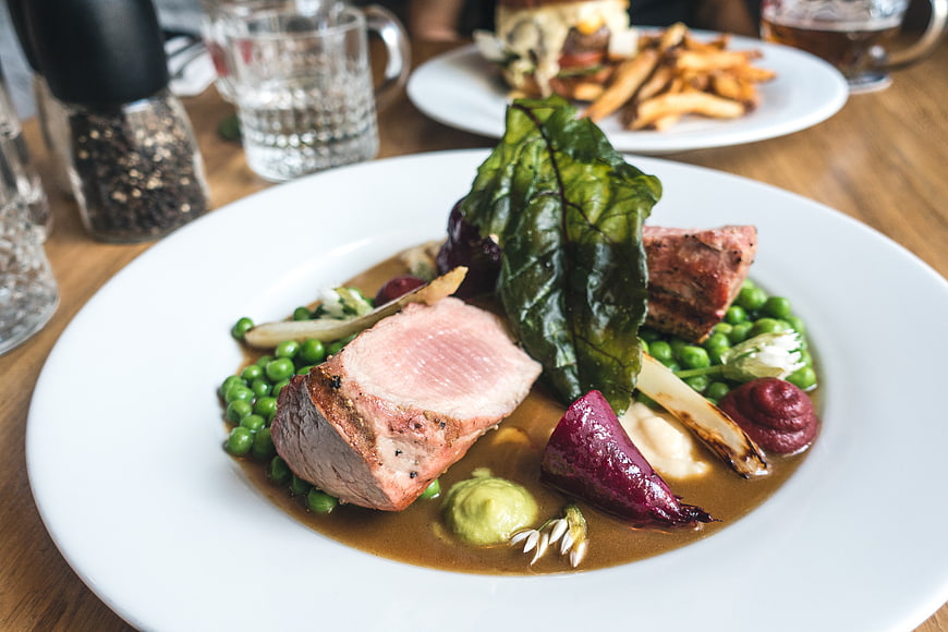 Seared pork tenderloin with peas, beetroot, and gravy on white plate