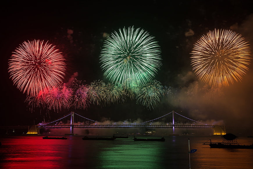 Colorful fireworks exploding over a suspension bridge at night