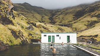People swimming in outdoor pool surrounded by green mountains