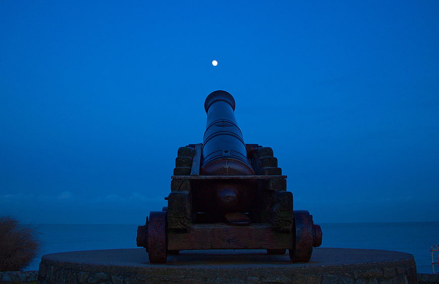 Historic Cannon Pointing at Moon Over Ocean at Night