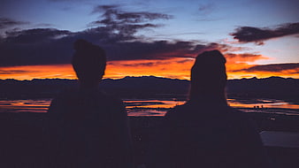 Silhouette of Two People Watching Sunset Over Mountains