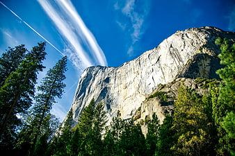 Majestic granite mountain cliff with pine trees and blue sky