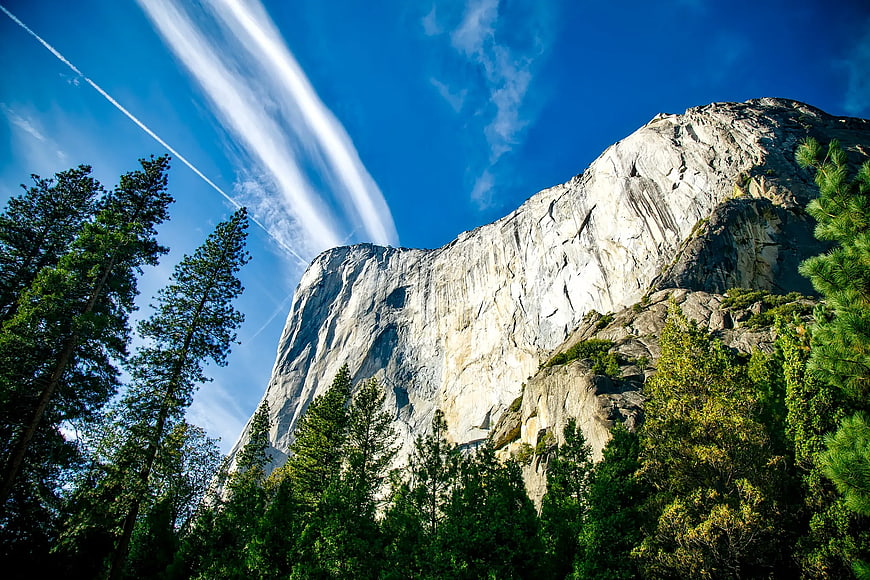 Majestic granite mountain cliff with pine trees and blue sky