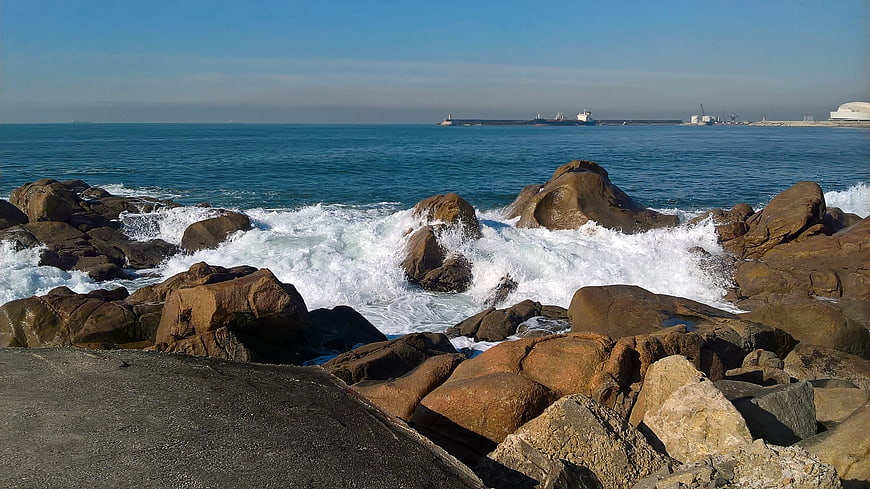 Rugged coastal rocks with crashing waves and distant port