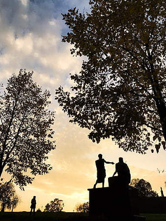 Silhouette of statues and trees against golden sunset sky