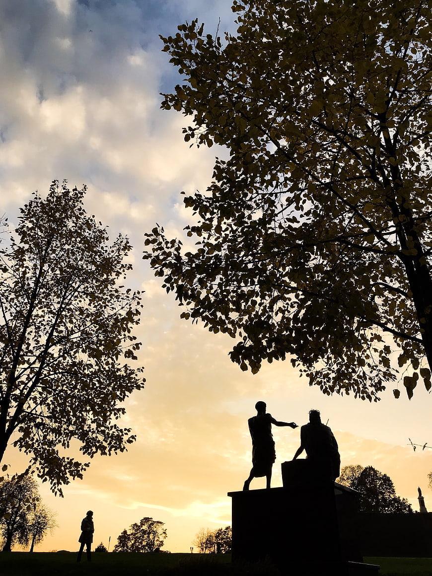 Silhouette of statues and trees against golden sunset sky