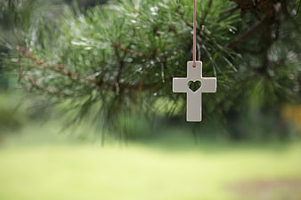 White cross with heart cutout hanging on pine branch