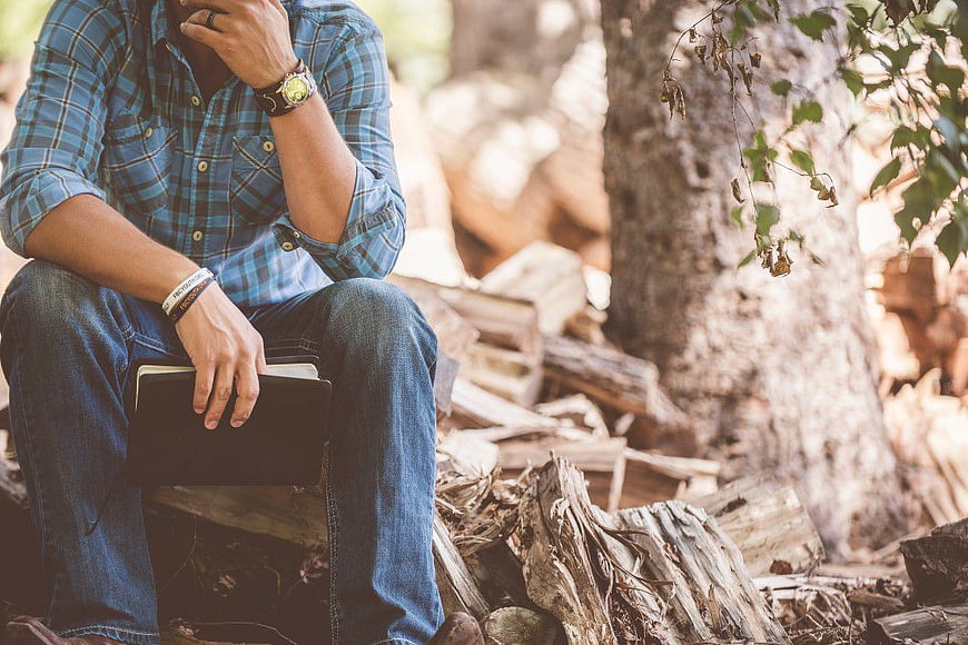 Man in Plaid Shirt Sitting in Forest with Notebook