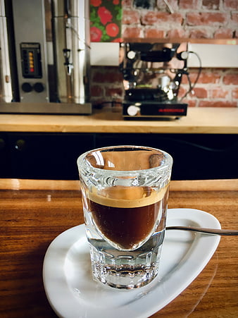 Espresso in a glass cup on a wooden table in a coffee shop