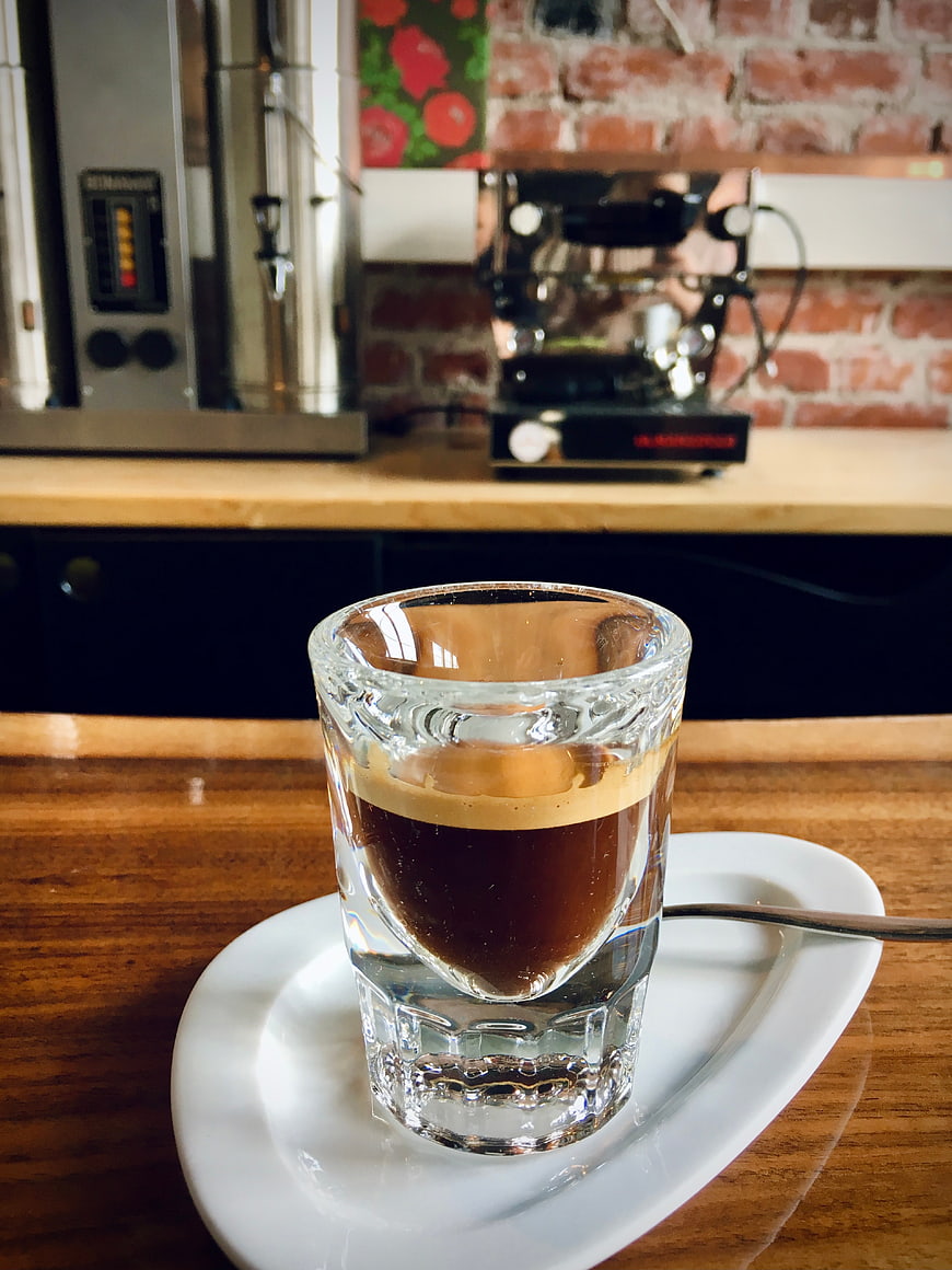Espresso in a glass cup on a wooden table in a coffee shop
