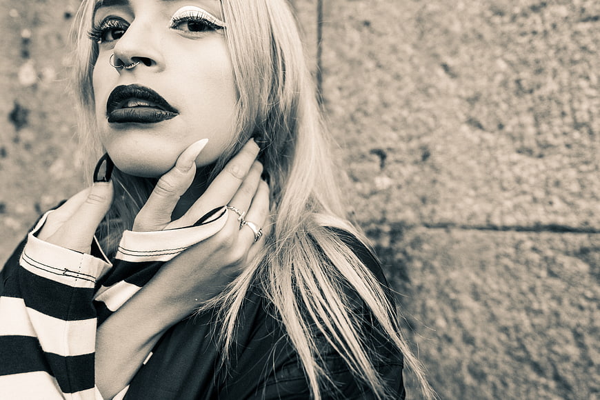 Gothic woman with dark makeup and striped shirt against stone wall