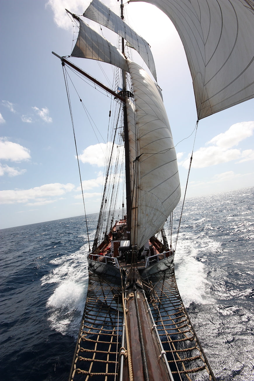 Tall ship sailing on open ocean with billowing white sails