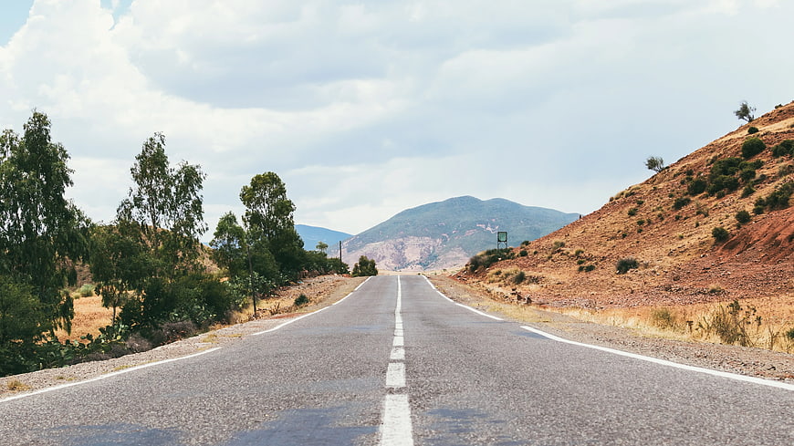 Empty asphalt road leading to mountains with trees and dry hills