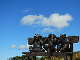 Three Wise Monkeys Sculpture on Bench Against Blue Sky