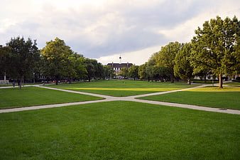 Wide green university quad with intersecting paths and historic building