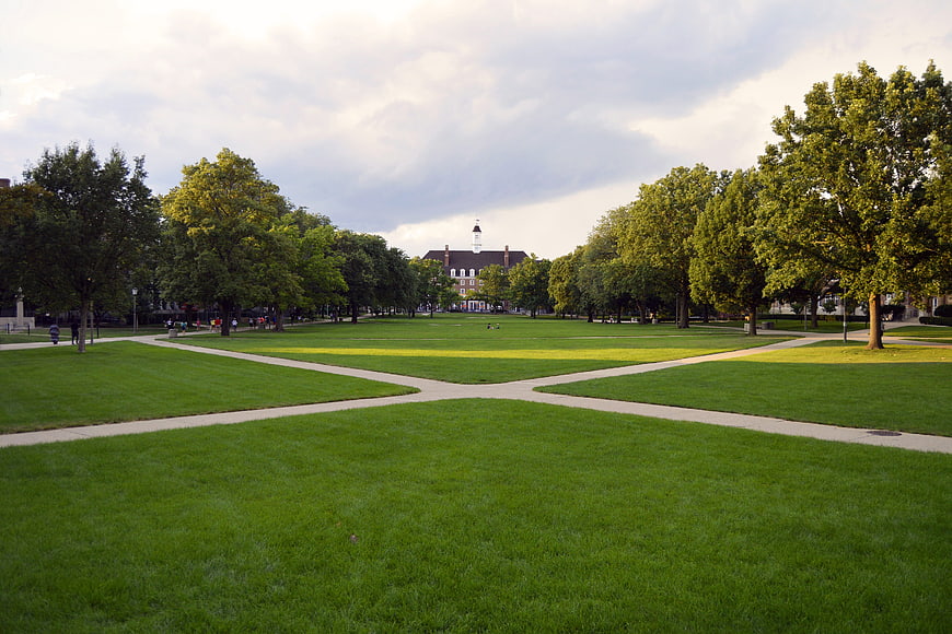Wide green university quad with intersecting paths and historic building