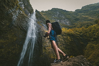 Male Hiker with Backpack and Camera Near Waterfall