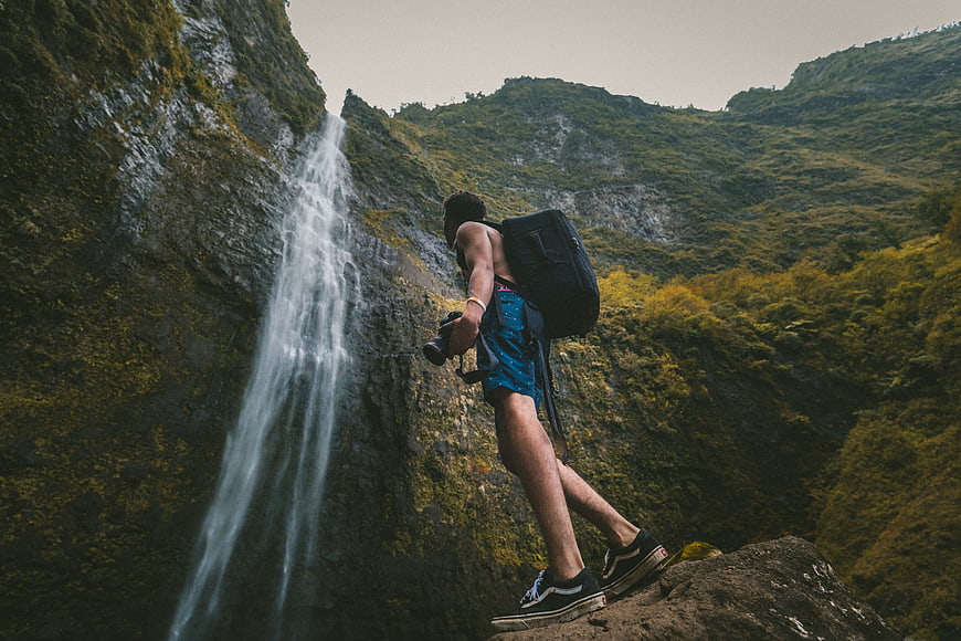 Male Hiker with Backpack and Camera Near Waterfall