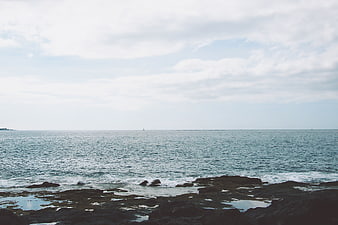 Serene Ocean View with Rocky Shore and Distant Sailboat