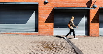 Woman walking past brick wall with garage doors