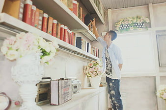 Young man reaching for book on shelf in vintage library