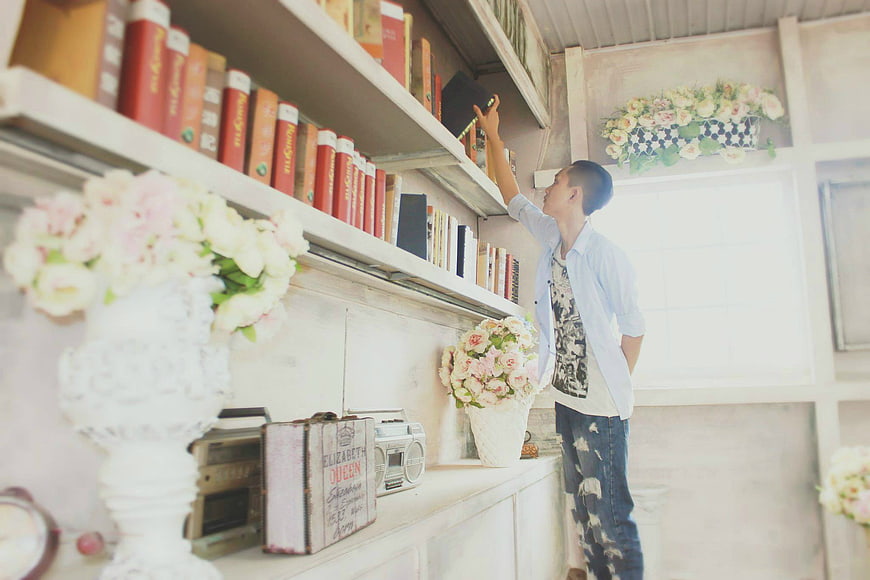 Young man reaching for book on shelf in vintage library