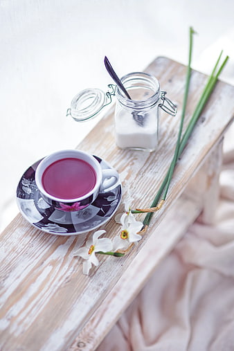 Pink fruit tea cup with sugar and white flowers on rustic wood