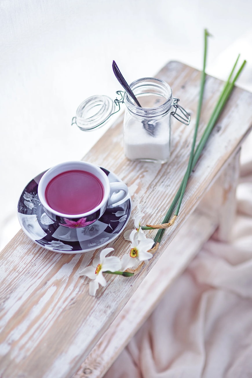 Pink fruit tea cup with sugar and white flowers on rustic wood