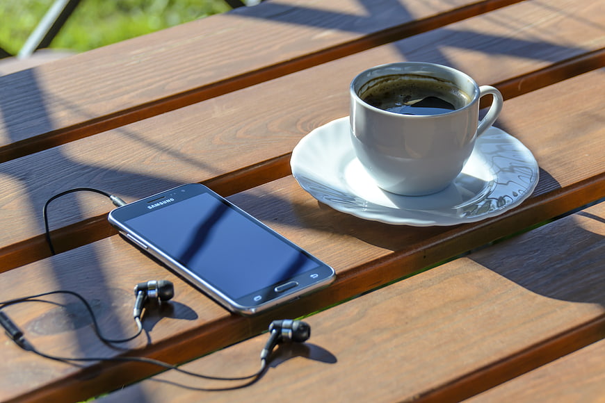 Smartphone with earphones and coffee cup on wooden table