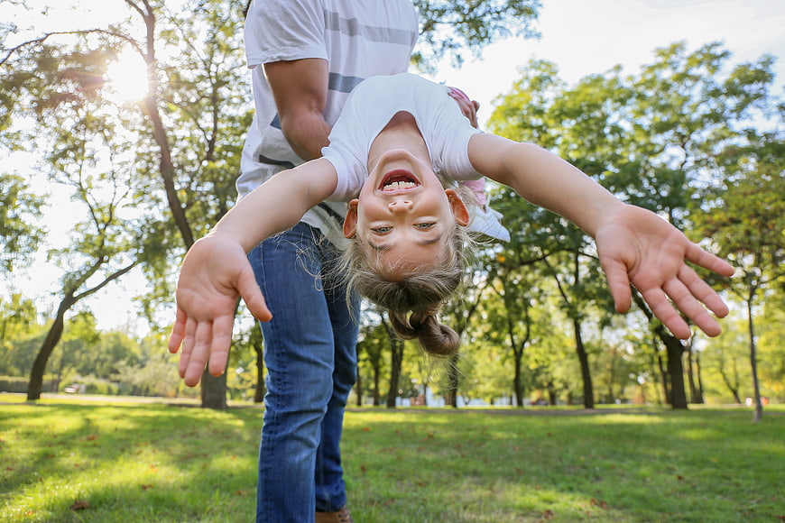 Happy Father Holding Daughter Upside Down in Park