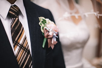 Close-up of groom's boutonniere and plaid tie with blurred bride