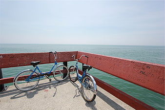 Two blue bicycles parked on a pier railing overlooking the ocean