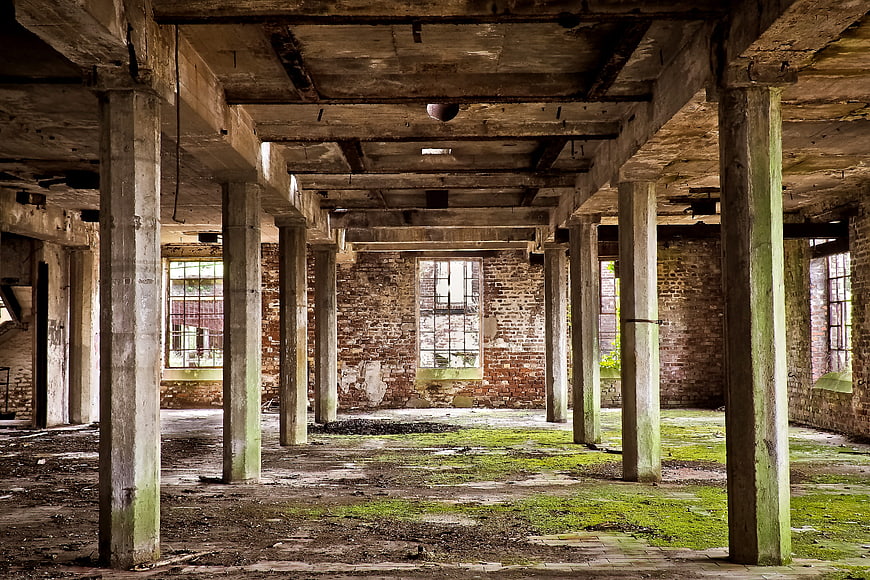 Abandoned industrial factory interior with mossy floor and concrete columns