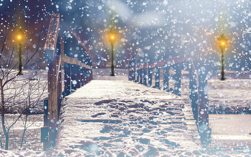 Snowy wooden bridge path with glowing street lamps in winter