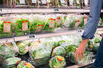 Hand selecting packaged lettuce in grocery store aisle