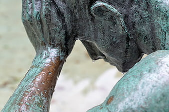 Close-up of weathered bronze statue head in despair