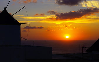 Silhouette of traditional windmill against vibrant sunset over ocean