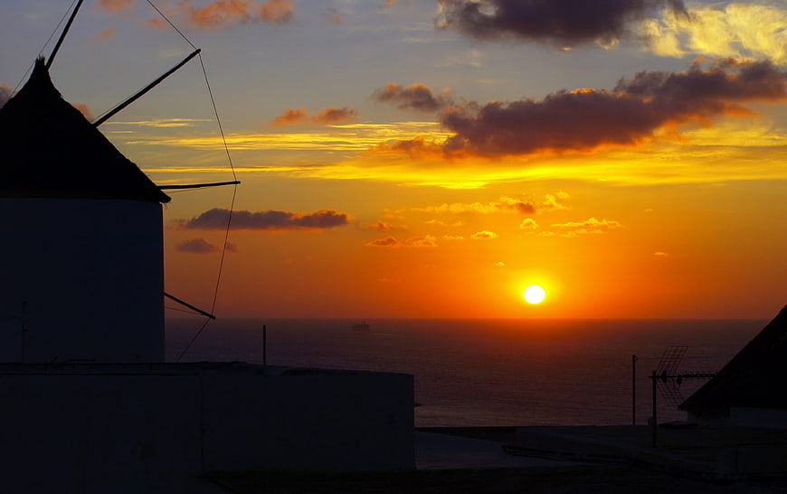 Silhouette of traditional windmill against vibrant sunset over ocean
