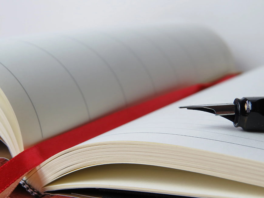 Close-up of fountain pen on open notebook with red ribbon