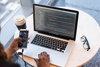 Developer coding on laptop with smartphone and coffee