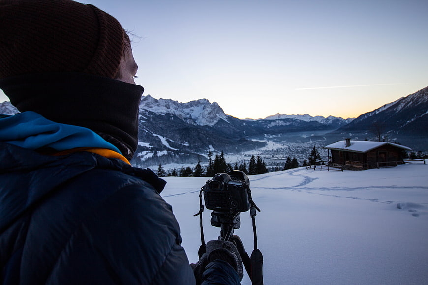 Photographer capturing snowy mountain landscape at dusk