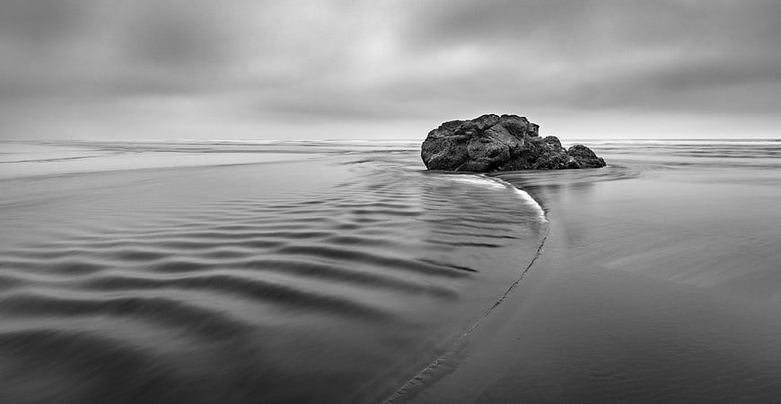 Solitary Rock on Smooth Black Sand Beach in Black and White