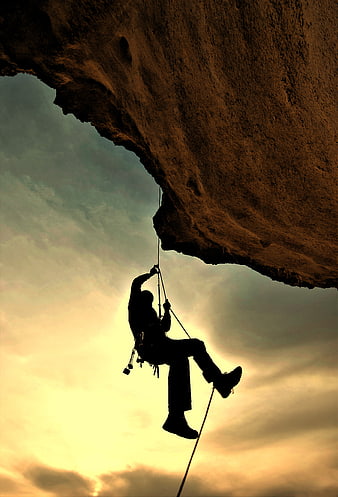 Silhouette of Rock Climber Hanging from Cliff at Sunset