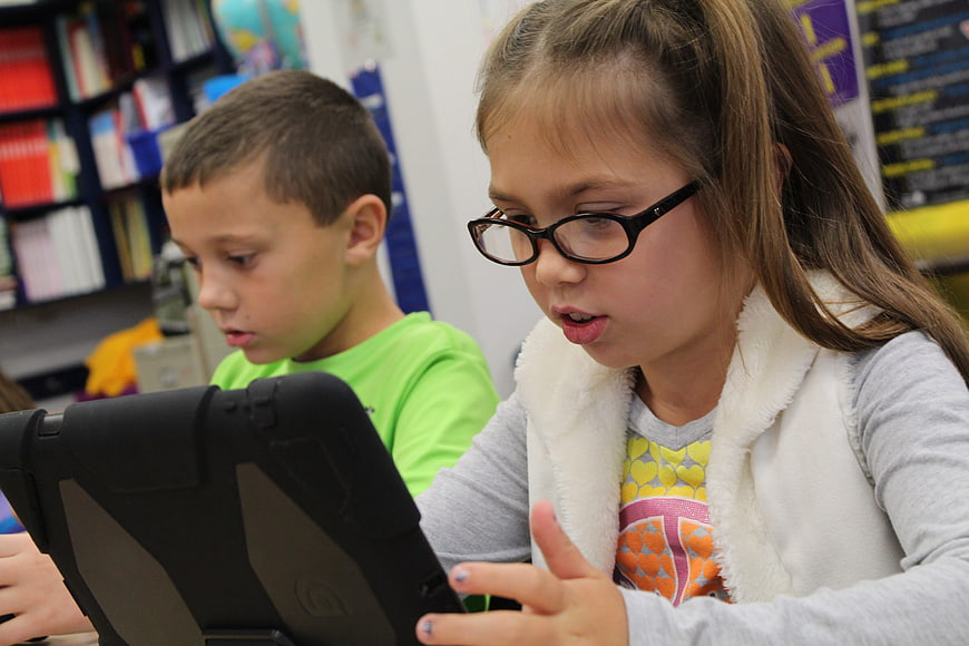 Young girl with glasses using tablet in classroom