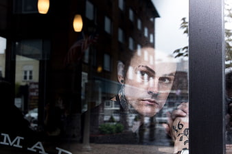 Man with tattoos looking through cafe window glass