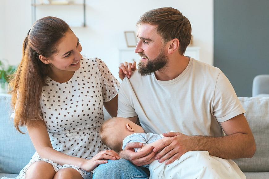 Young parents holding newborn baby on sofa at home