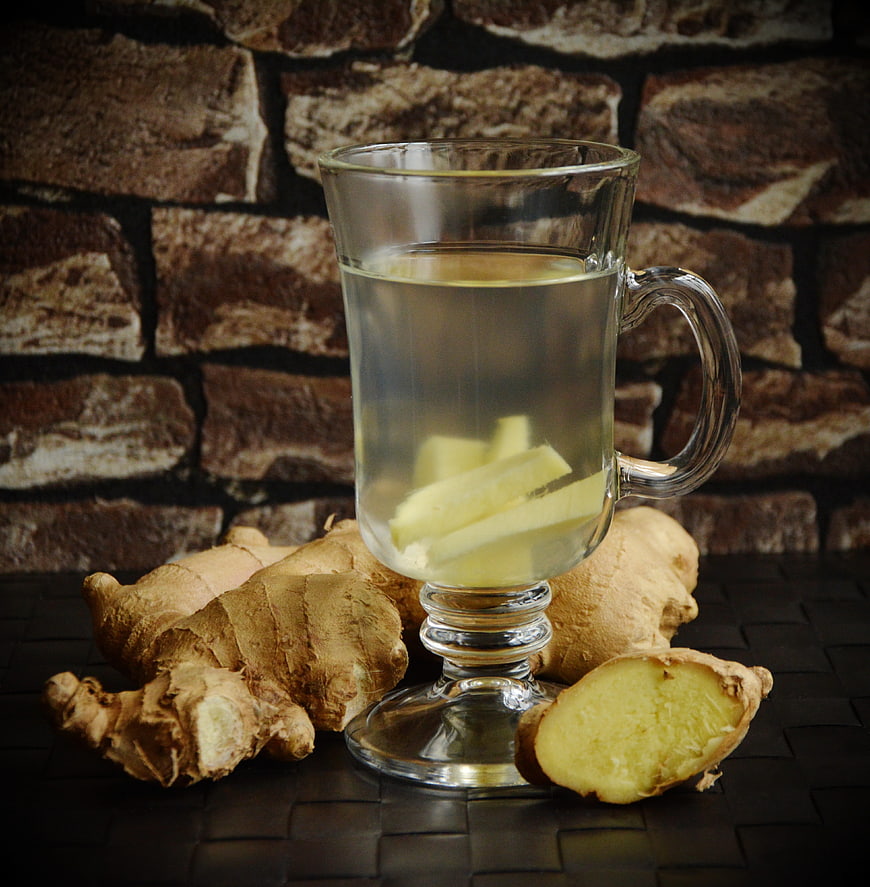 Glass mug of ginger tea with fresh ginger root on dark background